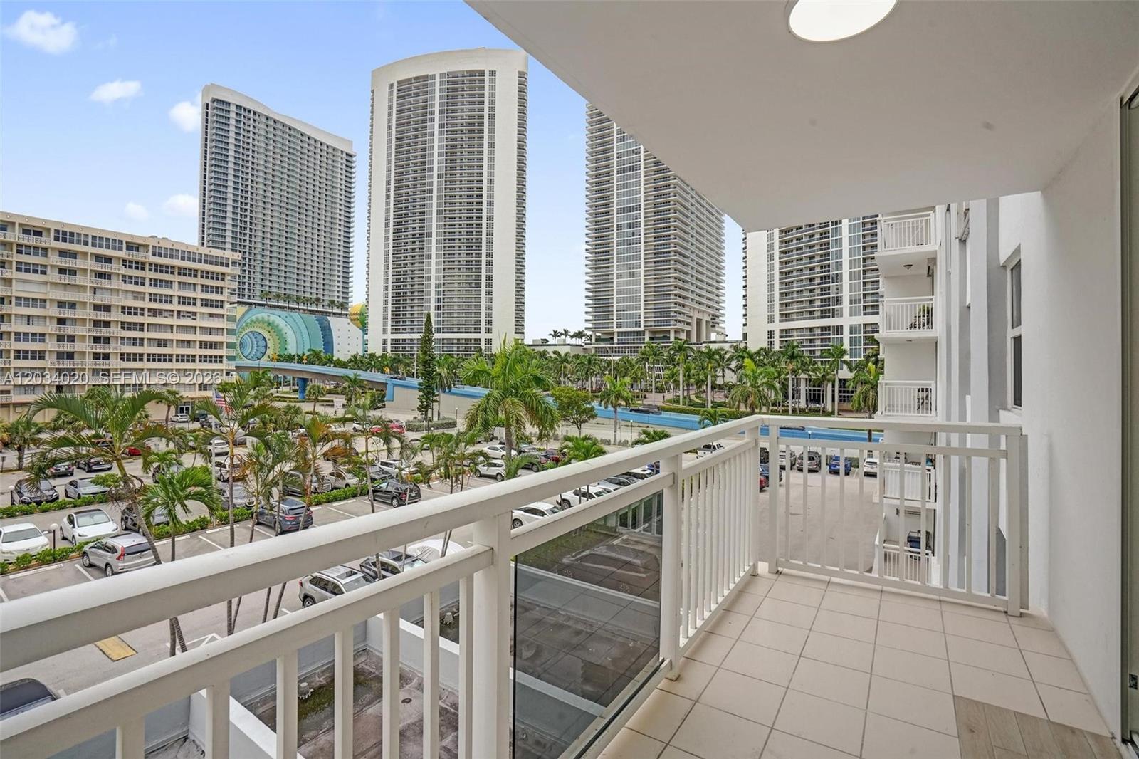 A balcony with white railings overlooks a parking lot and tall residential buildings — 1849 S Ocean Dr # 407, Hallandale Beach FL 33009, HALLANDALE BEACH, FL