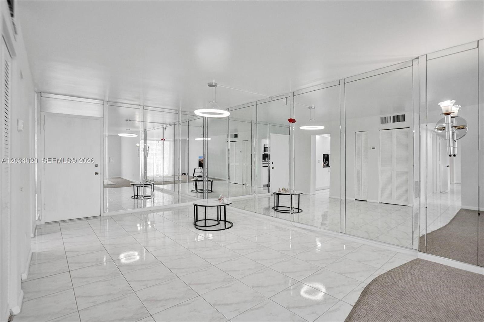 A bright, tiled room features extensive wall-to-wall mirrors and modern circular pendant lighting — 1849 S Ocean Dr # 407, Hallandale Beach FL 33009, HALLANDALE BEACH, FL