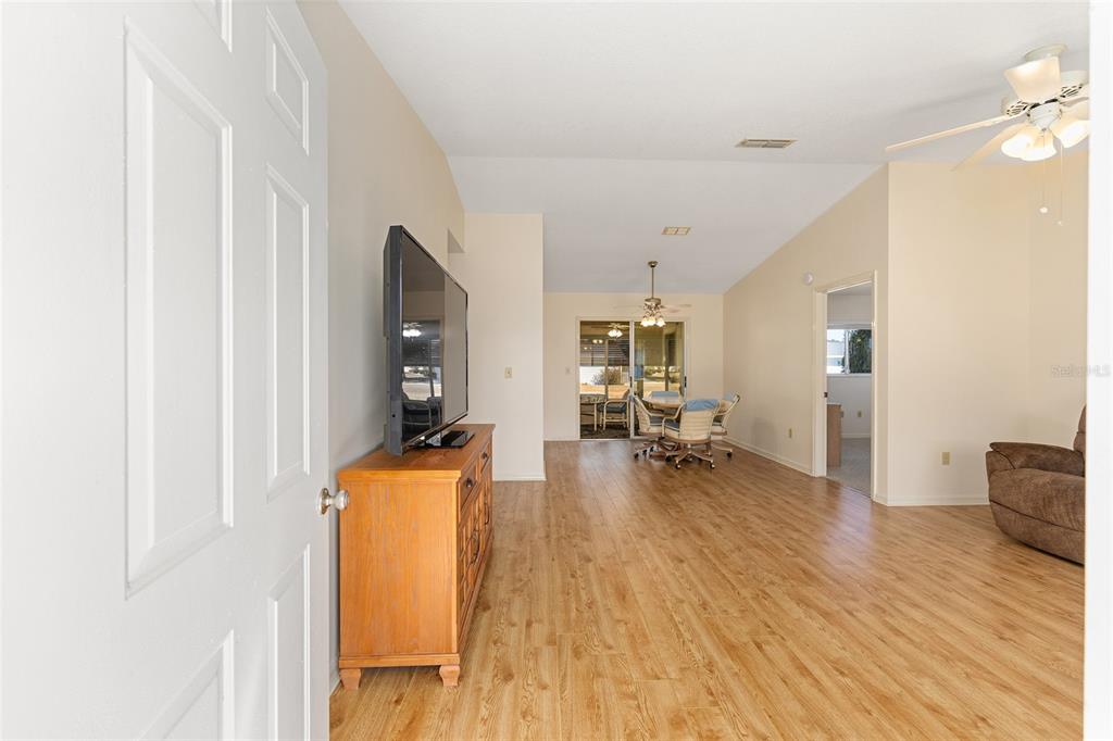 A living room with wood-look flooring, a television on a wooden console, and a dining area — 17929 SE 104TH TERRACE, SUMMERFIELD, FL