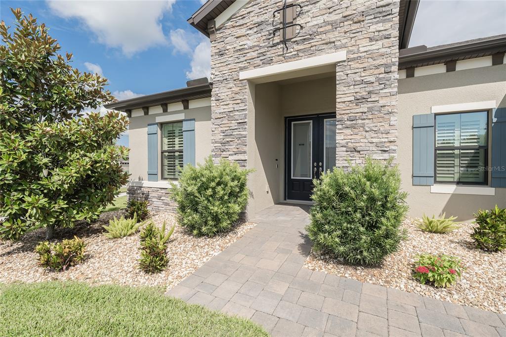 A stone-accented house exterior features a paved walkway leading to a dark double front door — 8687 BIRCHLEAF COURT COURT, LAND O LAKES, FL