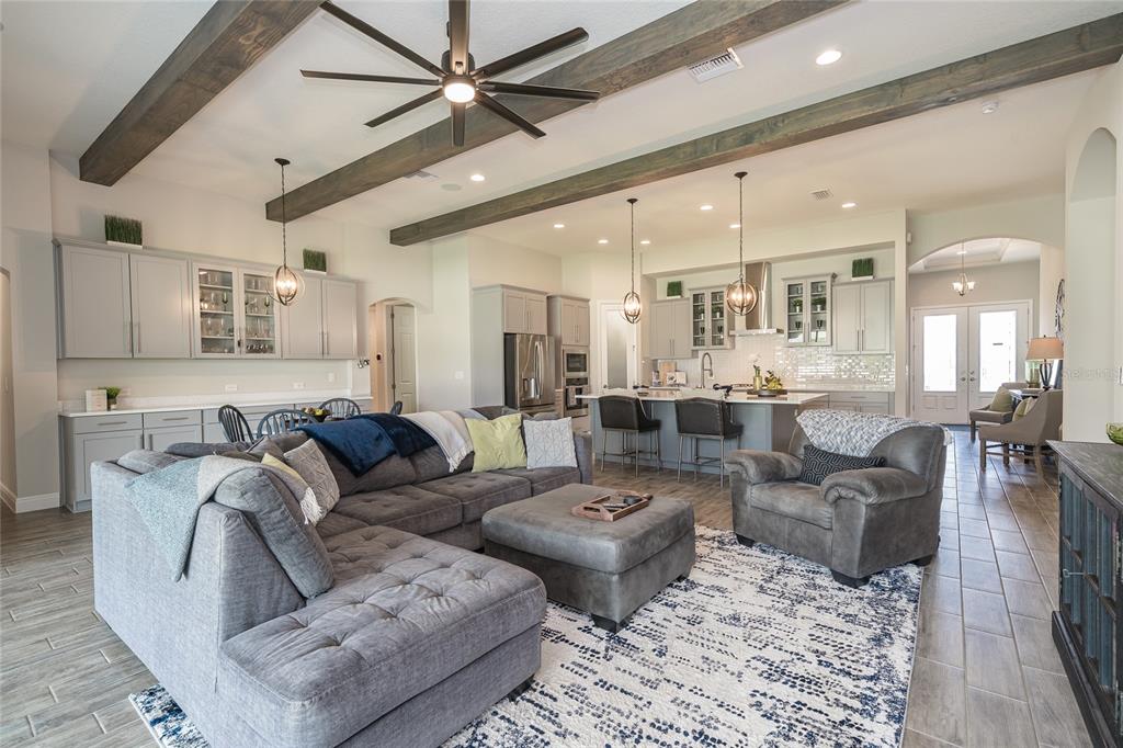 An open-concept living room and kitchen feature gray cabinetry, exposed ceiling beams, and tile flooring — 8687 BIRCHLEAF COURT COURT, LAND O LAKES, FL