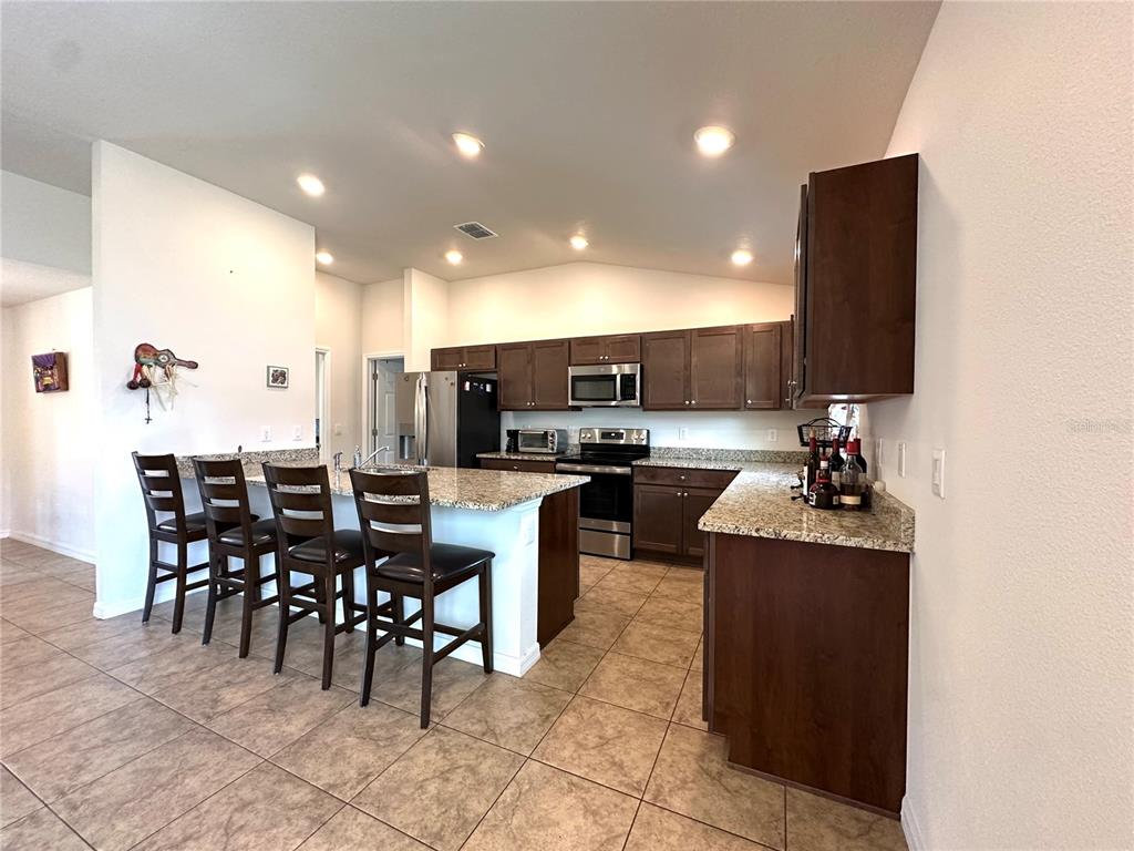 A kitchen with dark wood cabinets and granite countertops opens into a living room area — 15211 SW 65TH TERRACE ROAD, OCALA, FL