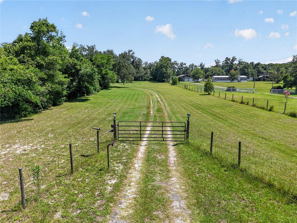 A metal gate opens to a dirt path leading through a grassy field toward houses — 2039 SW STATE ROAD 26, TRENTON, FL