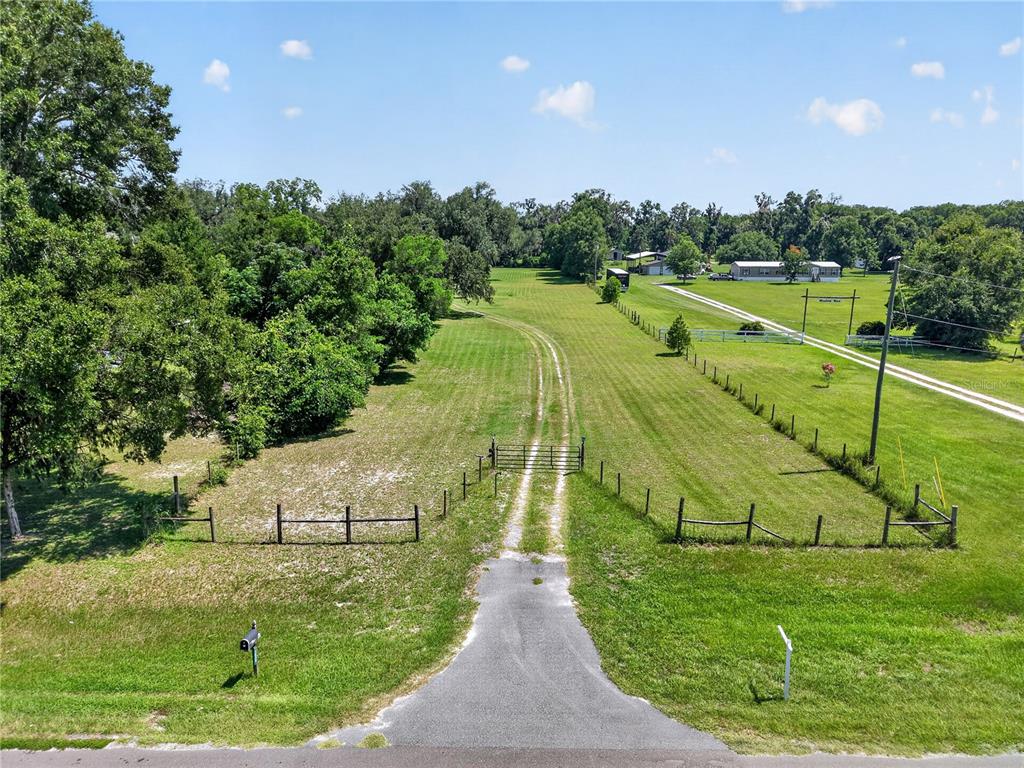 An aerial view shows a paved driveway leading to a gated entrance on a grassy lot — 2039 SW STATE ROAD 26, TRENTON, FL