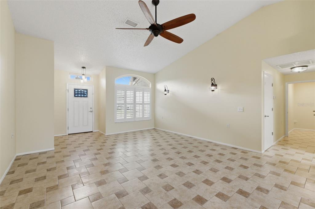 An empty room with light-colored walls, tiled flooring, a ceiling fan, and a front door — 6525 PINE WALK DRIVE, NEW PORT RICHEY, FL