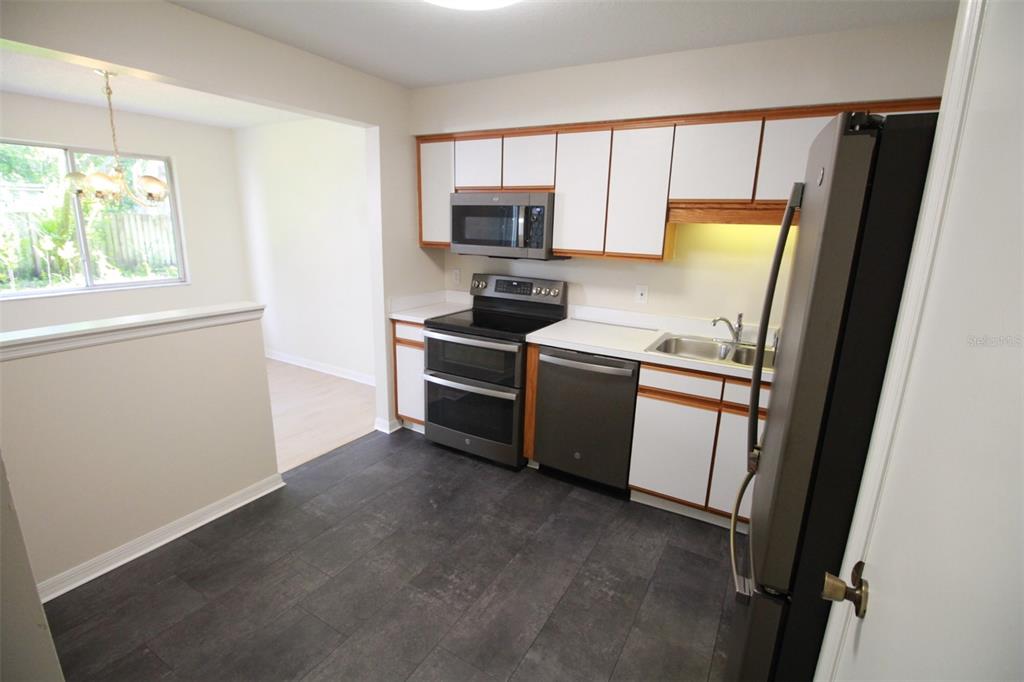 A kitchen features white cabinets with wood trim, stainless steel appliances, and dark tile flooring — 5301 WHITE CLIFF LANE UNIT 2, ORLANDO, FL