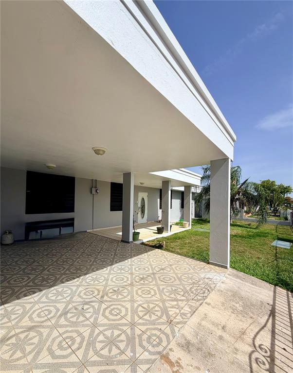 A covered patio with patterned tile flooring extends from a gray house with a lawn — #131 CALLE HARRINSON BASE RAMEY, AGUADILLA, PR