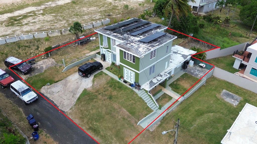 An aerial view shows a two-story green house with solar panels on the flat roof — PR-107 KM 2.2 INT CALLE SAN JOSE, AGUADILLA, PR