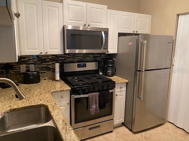 A kitchen features white cabinets, stainless steel appliances, and granite countertops — 2705 VIA MURANO UNIT 121, CLEARWATER, FL