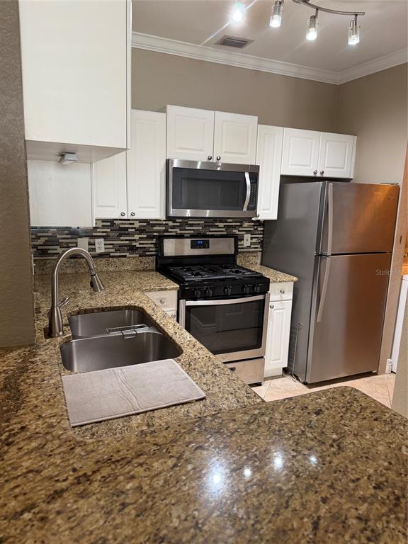 A kitchen features white cabinets, granite countertops, stainless steel appliances, and a tiled backsplash — 2705 VIA MURANO UNIT 121, CLEARWATER, FL