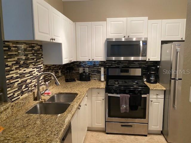 A kitchen features white cabinets, granite countertops, stainless steel appliances, and a tiled backsplash — 2705 VIA MURANO UNIT 121, CLEARWATER, FL