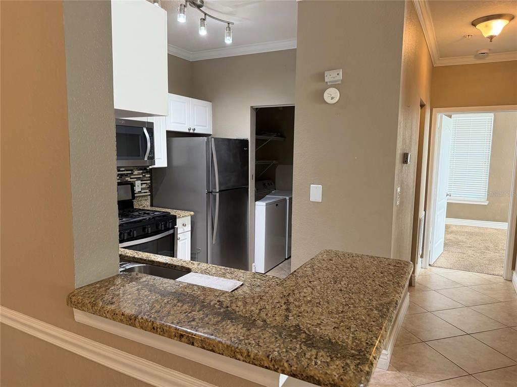 A kitchen with granite countertops, stainless steel appliances, and an adjacent laundry closet — 2705 VIA MURANO UNIT 121, CLEARWATER, FL