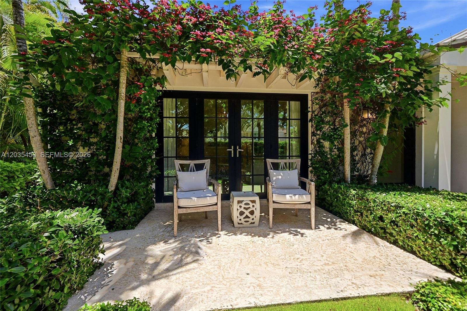 Two chairs and a small table sit on a stone patio beneath a flowering pergola — 135 Chilean Ave, Palm Beach FL 33480, PALM BEACH, FL