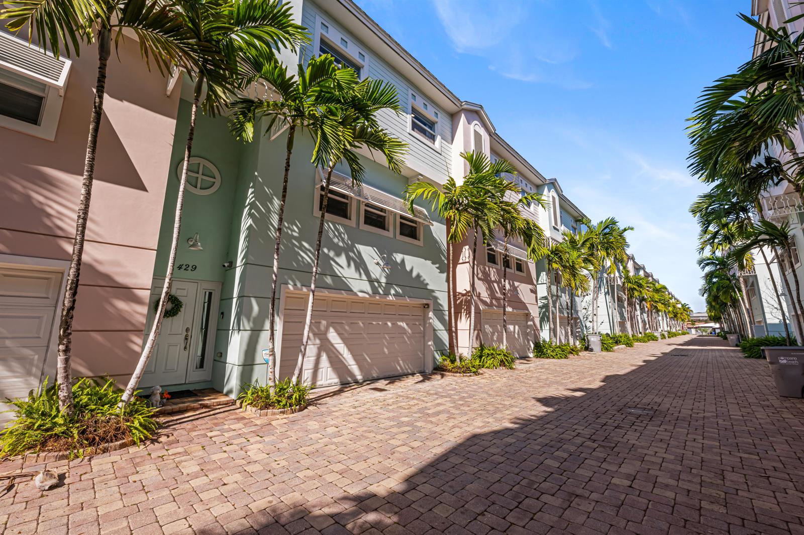 A row of pastel-colored townhouses with attached garages lines a paved brick driveway — 429 NE 1st Street, Pompano Beach FL 33060, POMPANO BEACH, FL