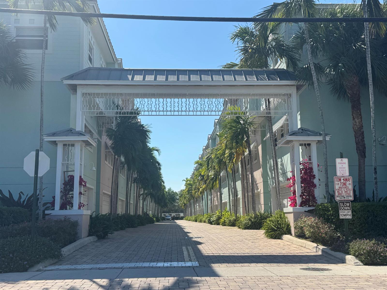 A paved driveway leads between two rows of pastel-colored townhomes under a decorative metal archway — 429 NE 1st Street, Pompano Beach FL 33060, POMPANO BEACH, FL