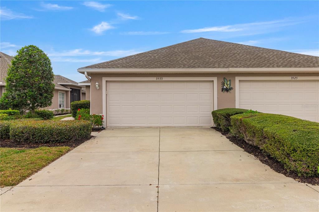 A beige two-car garage with a concrete driveway and manicured hedges in front — 3533 LAKEWOOD BOULEVARD, NORTH PORT, FL