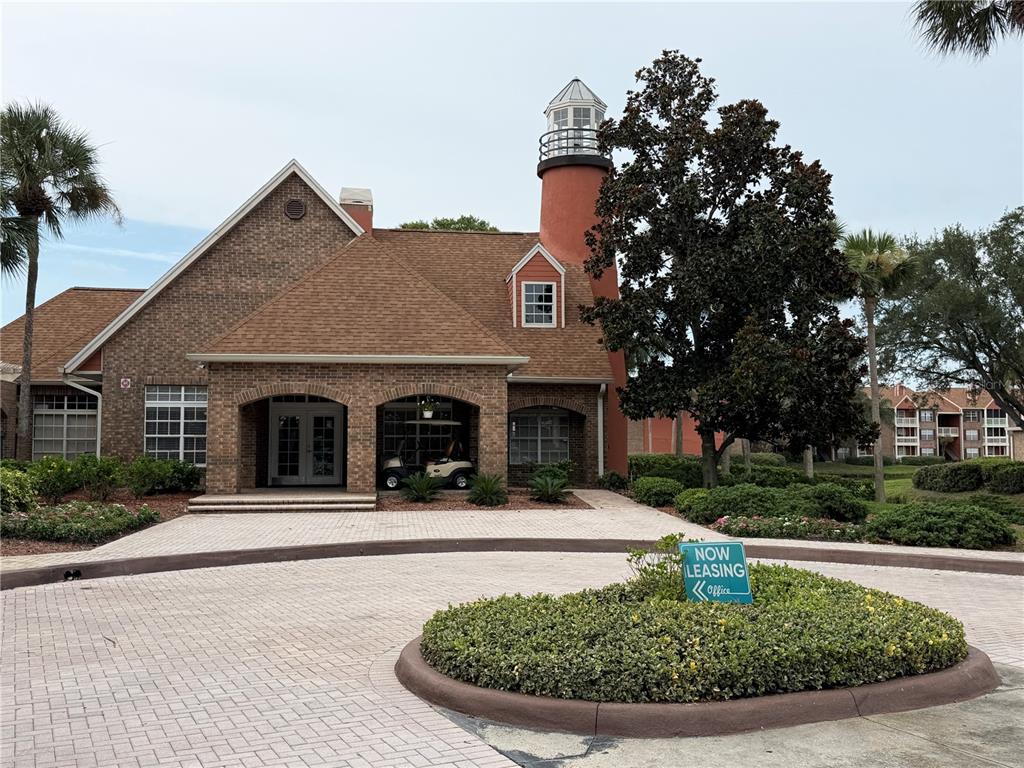 A brick building with a lighthouse-style tower stands behind a circular driveway and landscaping — 10200 GANDY BOULEVARD N UNIT 512, ST PETERSBURG, FL