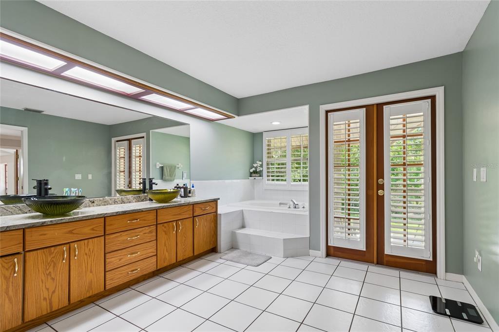 A bathroom features a double vanity with wood cabinets, a soaking tub, and glass-paned doors — 1055 RIVERSIDE RIDGE ROAD, TARPON SPRINGS, FL