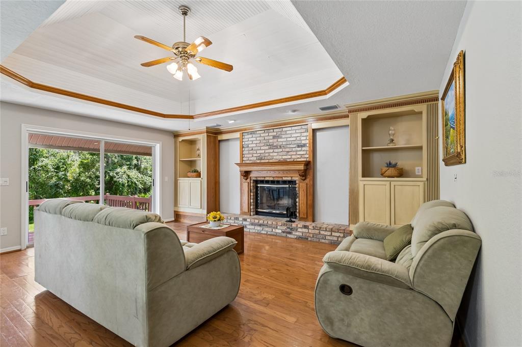 A living room features a brick fireplace, built-in shelving, hardwood floors, and a tray ceiling — 1055 RIVERSIDE RIDGE ROAD, TARPON SPRINGS, FL