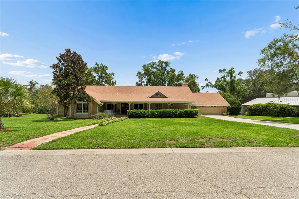 A single-story ranch-style house with a tan exterior, brown roof, and a large front lawn — 1055 RIVERSIDE RIDGE ROAD, TARPON SPRINGS, FL