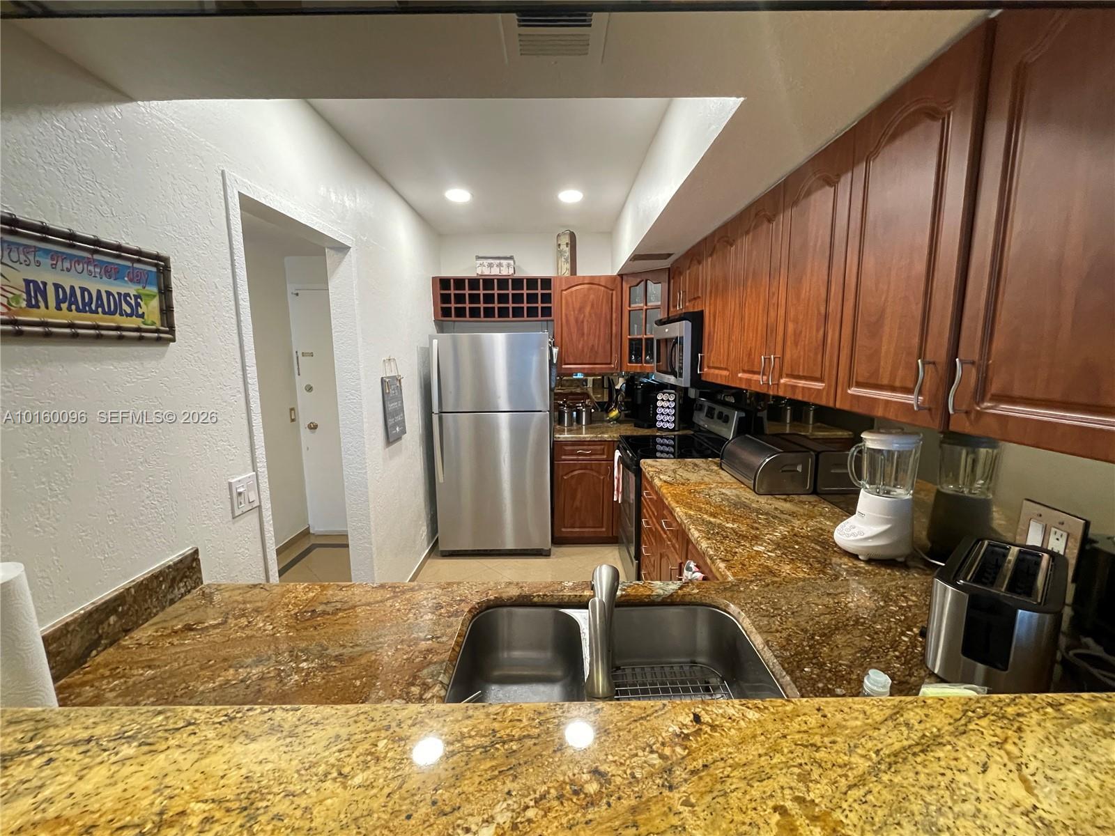 A kitchen features wood cabinets, granite countertops, stainless steel appliances, and a double-basin sink — 3505 S Ocean Dr # 105, Hollywood FL 33019, HOLLYWOOD, FL