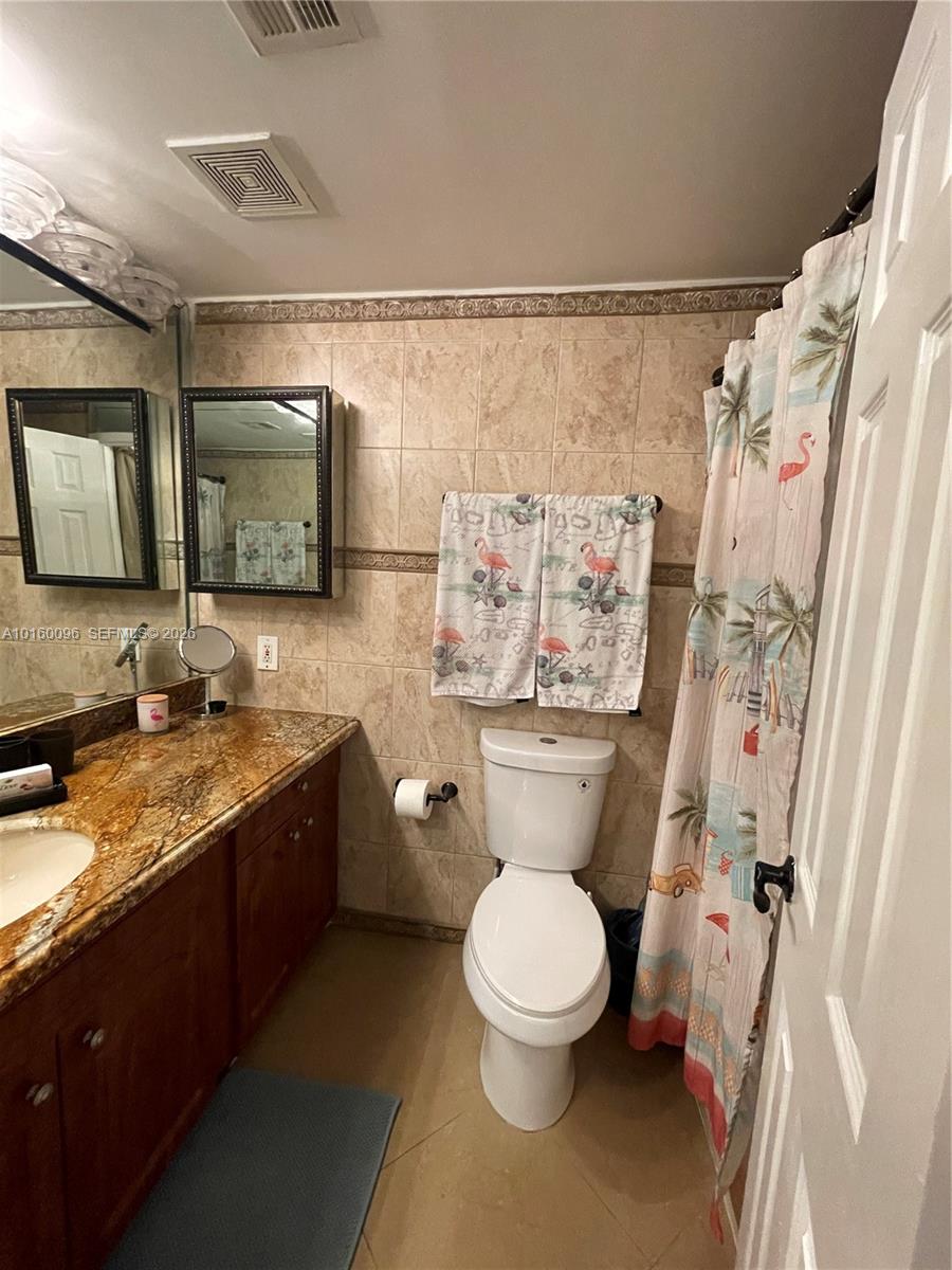 A bathroom features a granite vanity, tile walls, a toilet, and a flamingo-patterned shower curtain — 3505 S Ocean Dr # 105, Hollywood FL 33019, HOLLYWOOD, FL