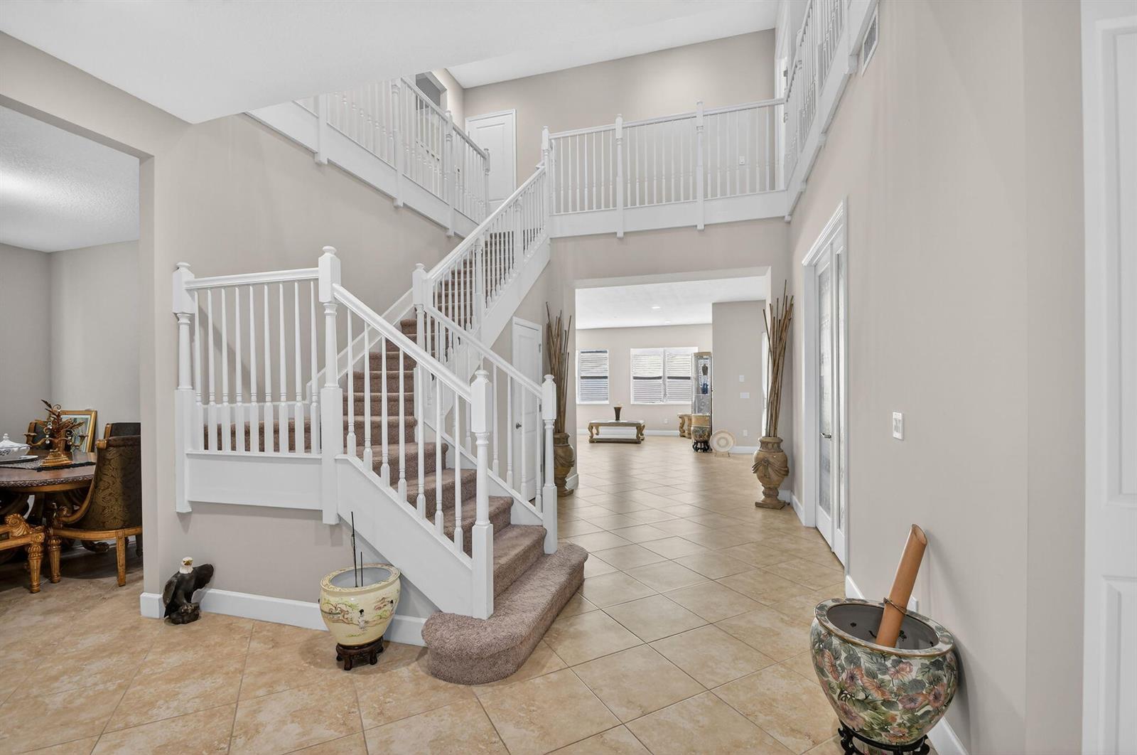 A foyer features a carpeted staircase with white railings, tile flooring, and a high ceiling — 5632 Liberty Lane, Westlake FL 33470, WESTLAKE, FL