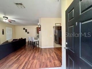 A view from an entryway into a living room with wood-look flooring and bar stools — 1470 BROKEN OAK DRIVE UNIT 27C, WINTER GARDEN, FL