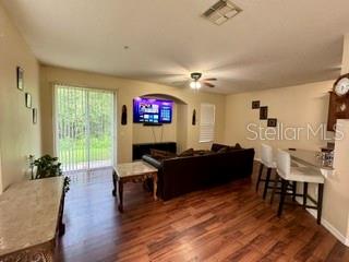A living room features wood-look flooring, a dark sofa, a television, and a sliding door — 1470 BROKEN OAK DRIVE UNIT 27C, WINTER GARDEN, FL