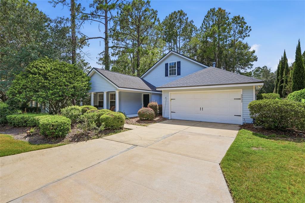 A light blue house with a two-car garage and a concrete driveway sits among trees — 3052 SW 94TH STREET, GAINESVILLE, FL