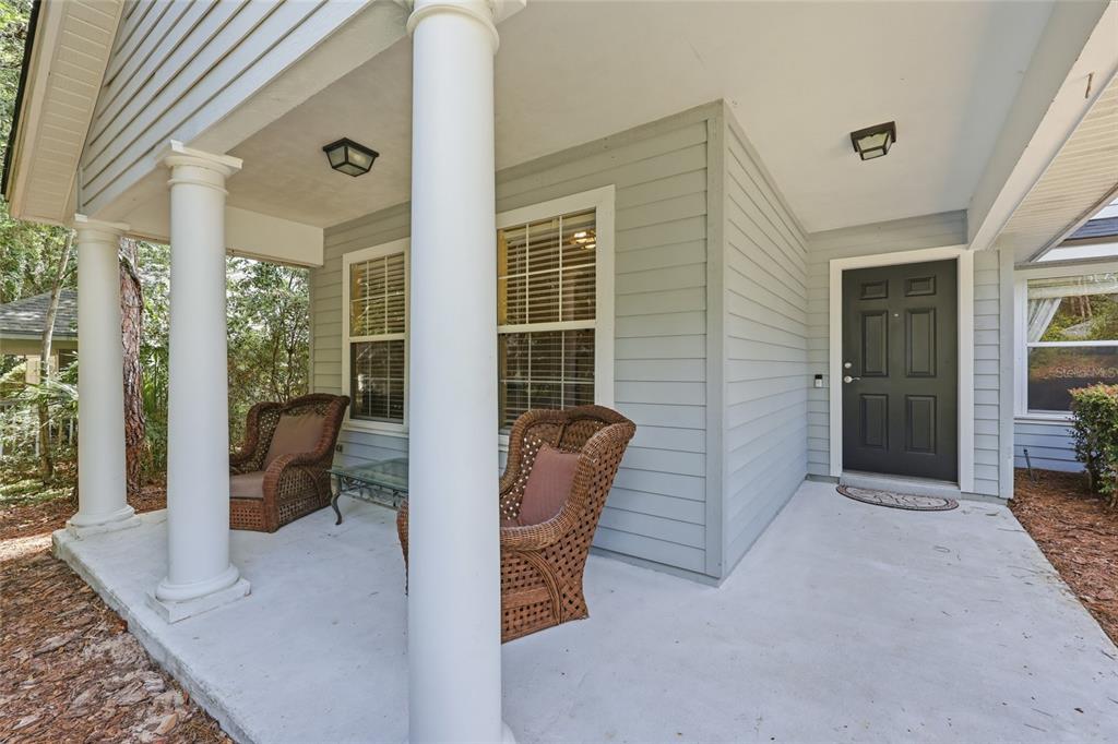 A covered front porch features light gray siding, white columns, and two wicker chairs — 3052 SW 94TH STREET, GAINESVILLE, FL