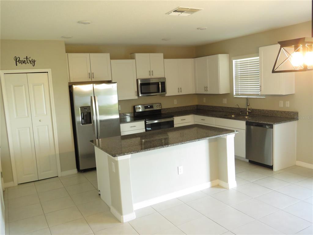 A kitchen features white cabinets, stainless steel appliances, granite countertops, and a central island — 15518 MILLER CREEK DRIVE, SUN CITY CENTER, FL