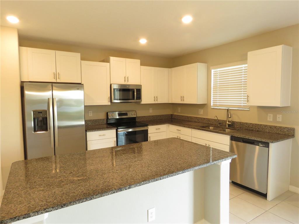 A kitchen features white cabinets, granite countertops, stainless steel appliances, and a central island — 15518 MILLER CREEK DRIVE, SUN CITY CENTER, FL