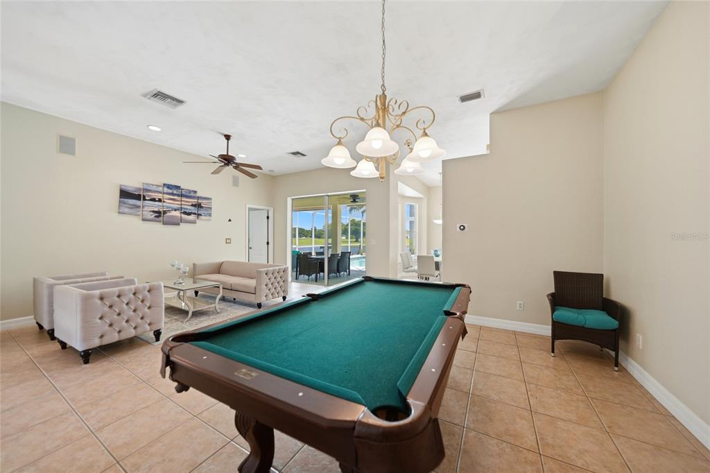 A spacious room features a pool table, a seating area, and a view of a pool — 1511 NW 29TH PLACE, CAPE CORAL, FL