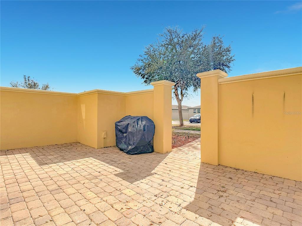 A paved patio features a covered grill and tan stucco walls under a clear sky — 2380 BELLA VISTA DRIVE, DAVENPORT, FL