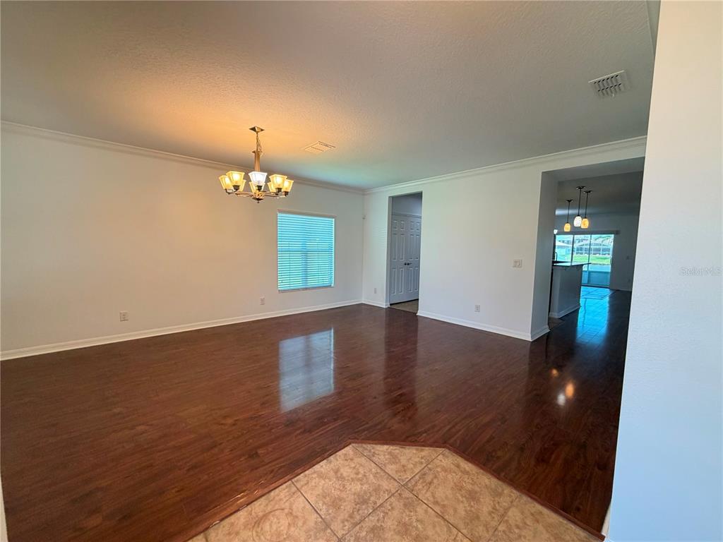 A bright, empty living room features dark wood-look flooring, white walls, and a chandelier — 3437 BRANT STREET, ST CLOUD, FL