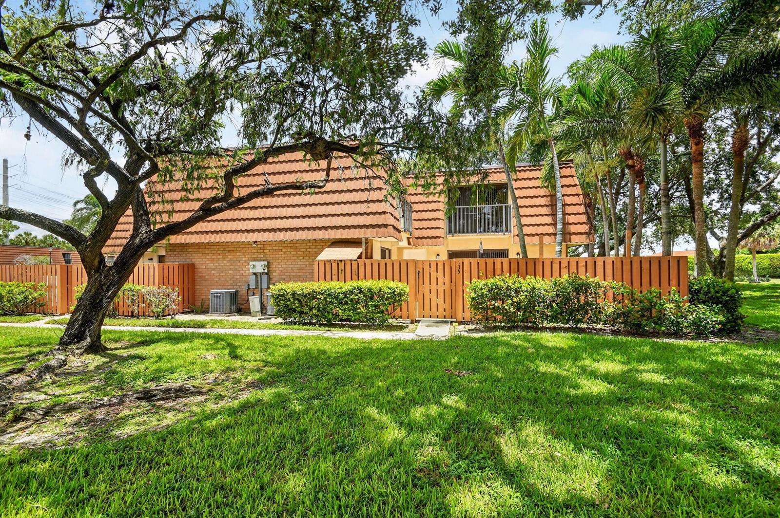 A two-story townhouse with a brown tile roof, brick exterior, and a wooden privacy fence — 135 Heritage Way, West Palm Beach FL 33407, WEST PALM BEACH, FL