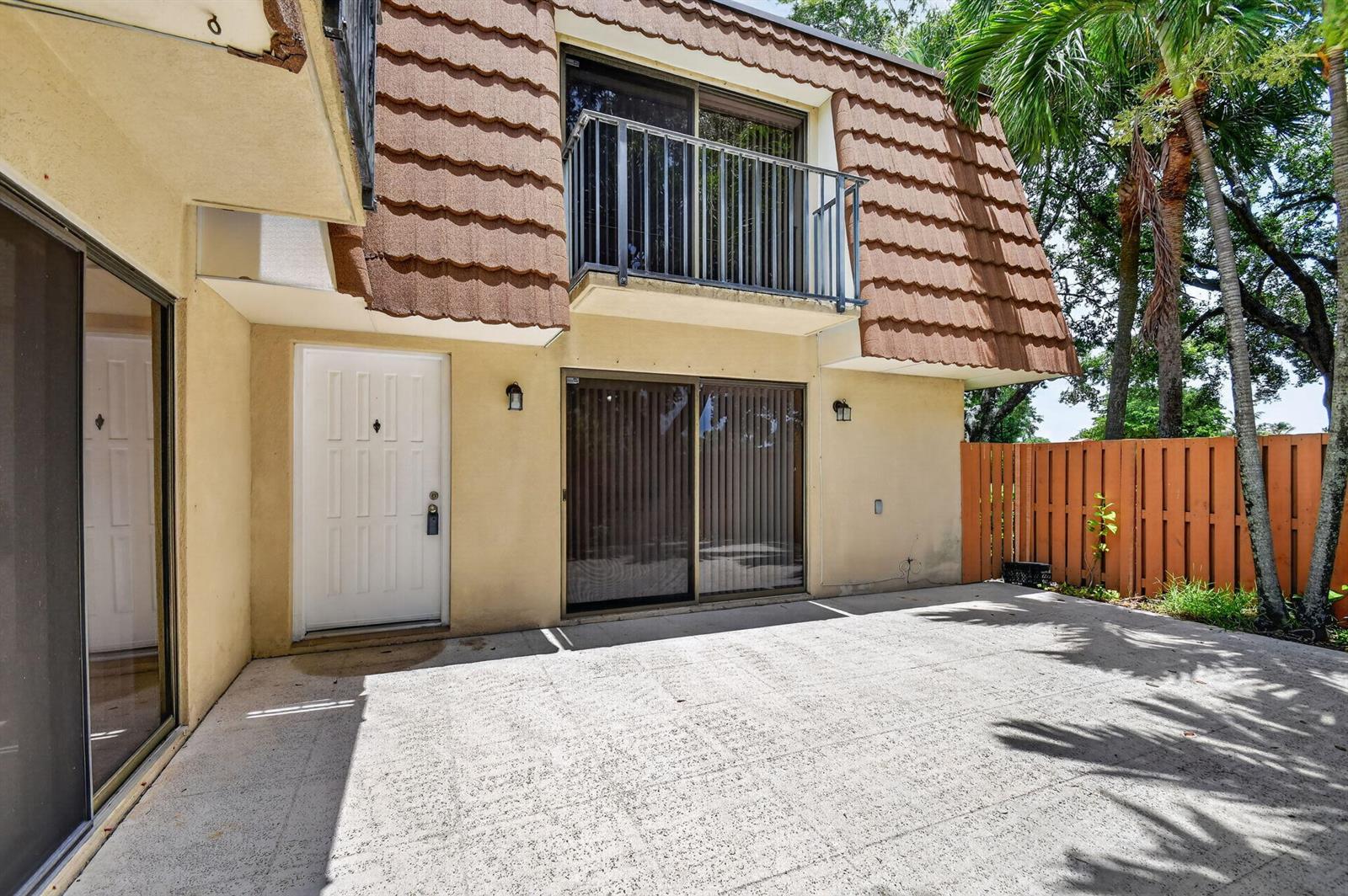 A patio area sits in front of a two-story building with a balcony and sliding doors — 135 Heritage Way, West Palm Beach FL 33407, WEST PALM BEACH, FL