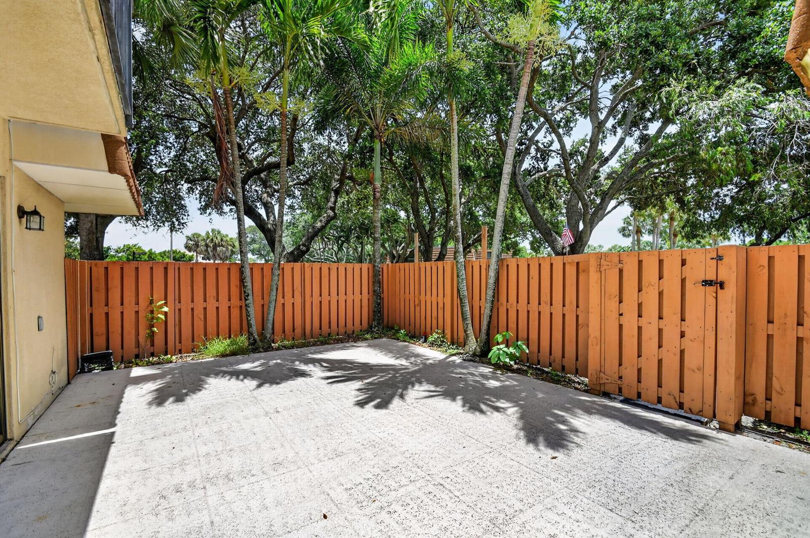 A concrete patio enclosed by a wooden fence with palm trees and mature trees — 135 Heritage Way, West Palm Beach FL 33407, WEST PALM BEACH, FL