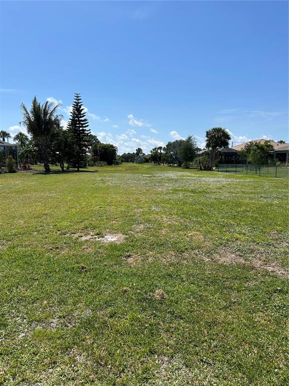 A large, grassy vacant lot with scattered trees under a clear blue sky — 7357 PARKINSONIA, PUNTA GORDA, FL