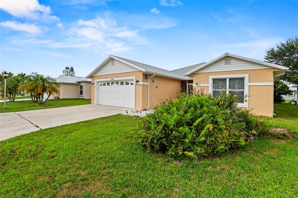 A single-story house with a white garage door, tan stucco walls, and a metal roof — 6648 GAVIOTA, FORT PIERCE, FL