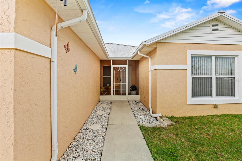 A concrete walkway leads to a screened front entryway of a tan stucco house — 6648 GAVIOTA, FORT PIERCE, FL