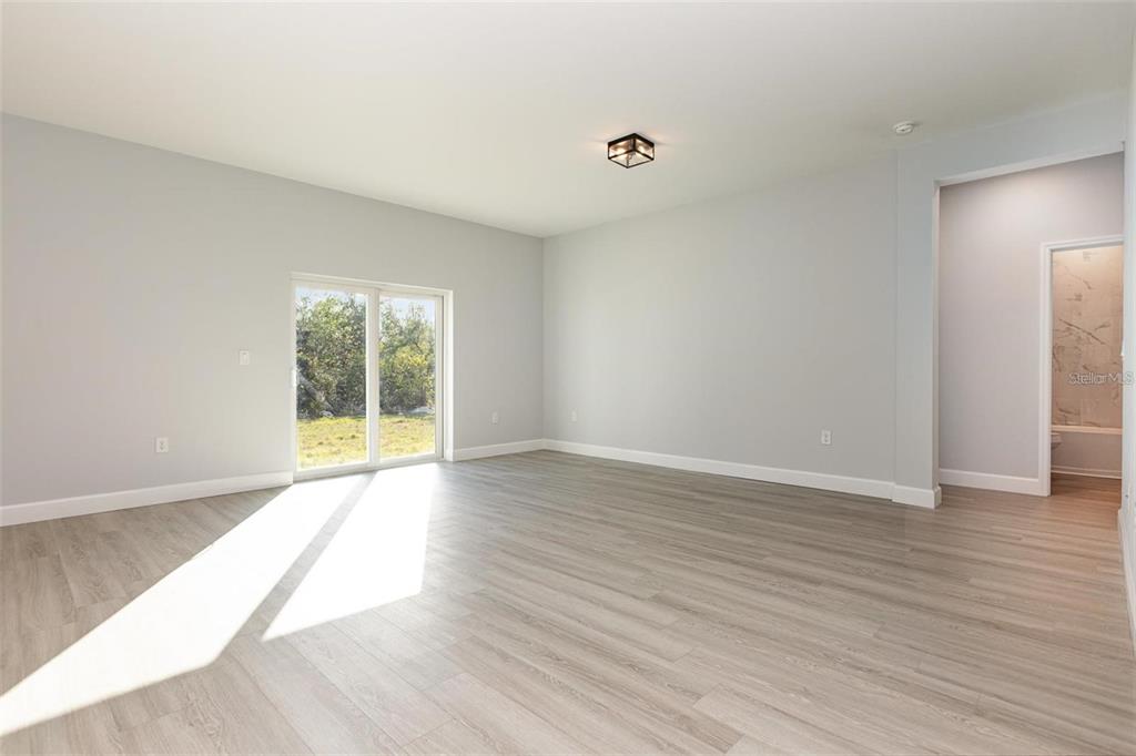 An empty room with light gray walls, wood-look flooring, and a sliding glass door — 13451 KAPLAN TERRACE, PORT CHARLOTTE, FL
