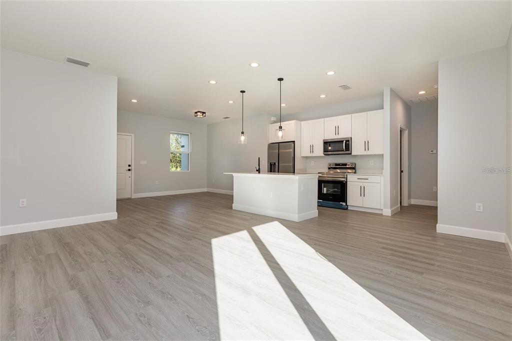 A modern kitchen with white cabinets and a central island opens into a living area — 13451 KAPLAN TERRACE, PORT CHARLOTTE, FL