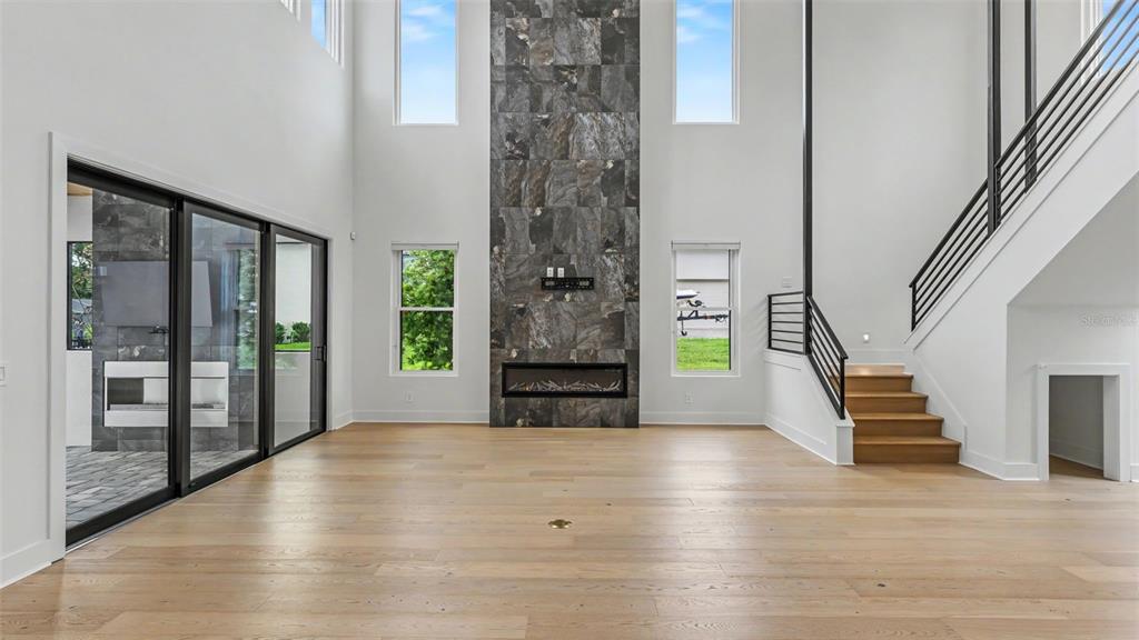 A spacious living room features light wood floors, a tall stone fireplace, and a staircase — 5411 DELPHI HILLS CIRCLE, LAKELAND, FL