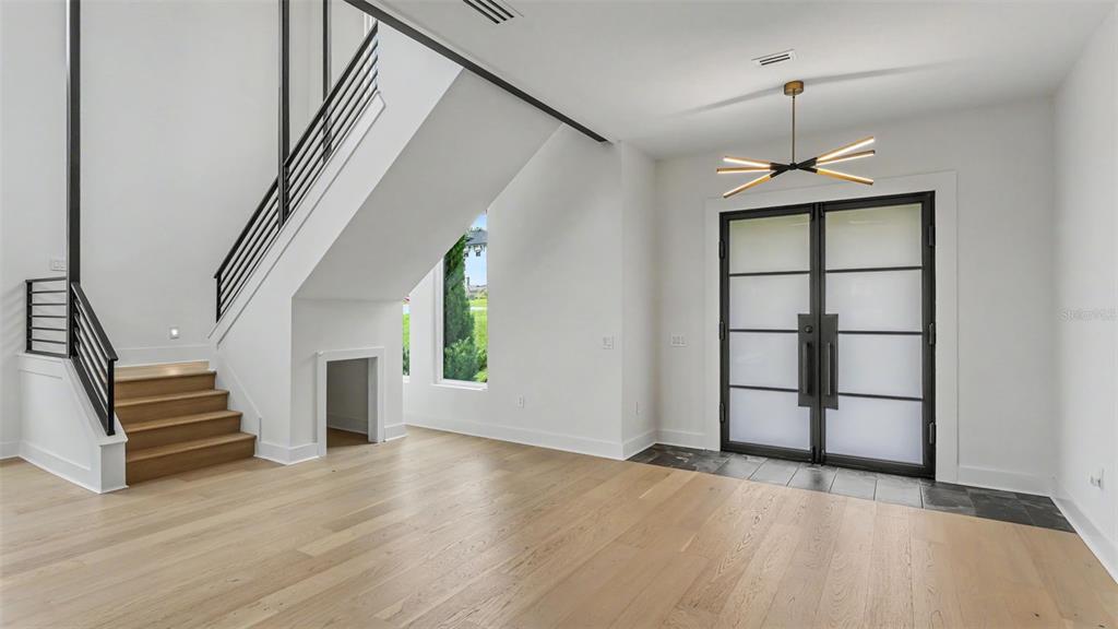 A bright foyer features light wood floors, a modern chandelier, and a black-railed staircase — 5411 DELPHI HILLS CIRCLE, LAKELAND, FL