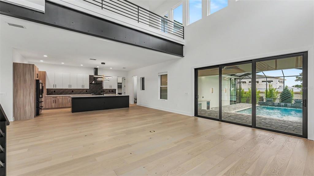 A modern open-concept living area features light wood floors, a black kitchen island, and pool — 5411 DELPHI HILLS CIRCLE, LAKELAND, FL