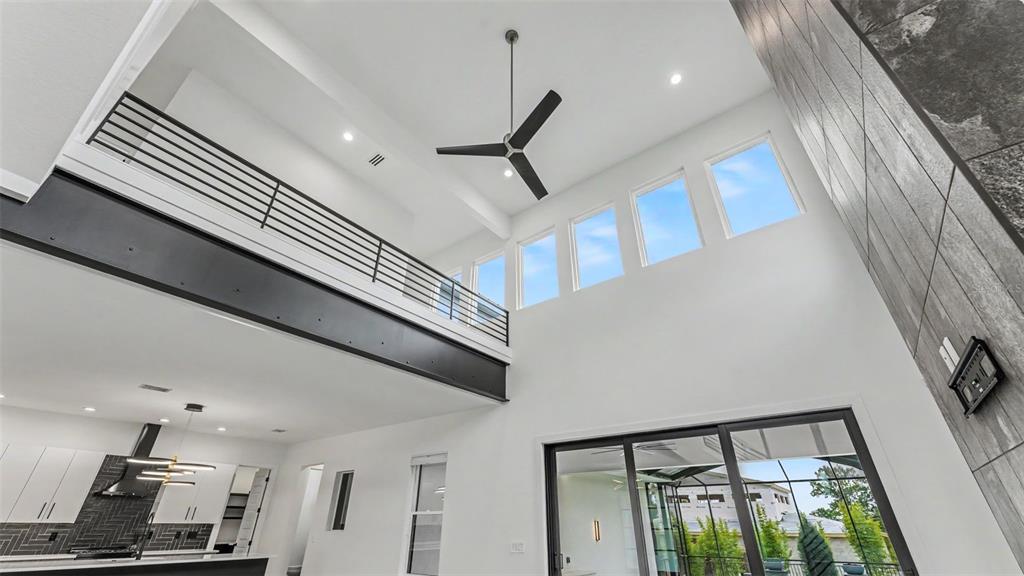 A modern living room features a high ceiling, a black metal railing, and large windows — 5411 DELPHI HILLS CIRCLE, LAKELAND, FL