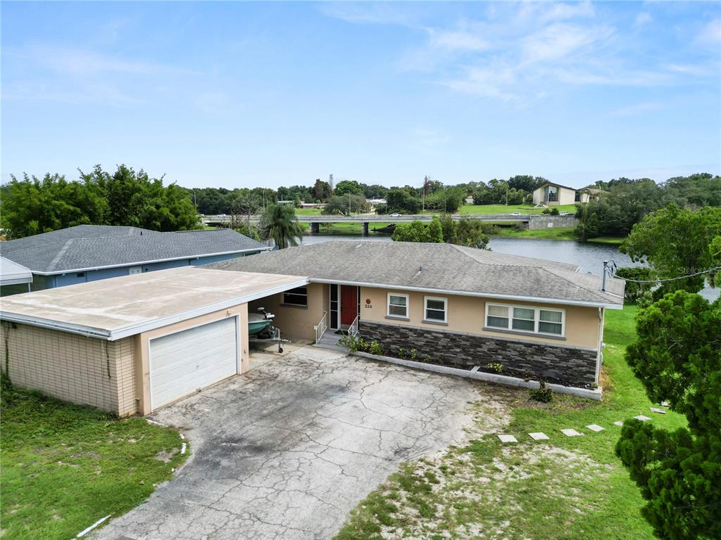 An elevated view of a single-story house with a carport, stone facade, and waterfront backyard — 228 W LAKE INA DRIVE, WINTER HAVEN, FL