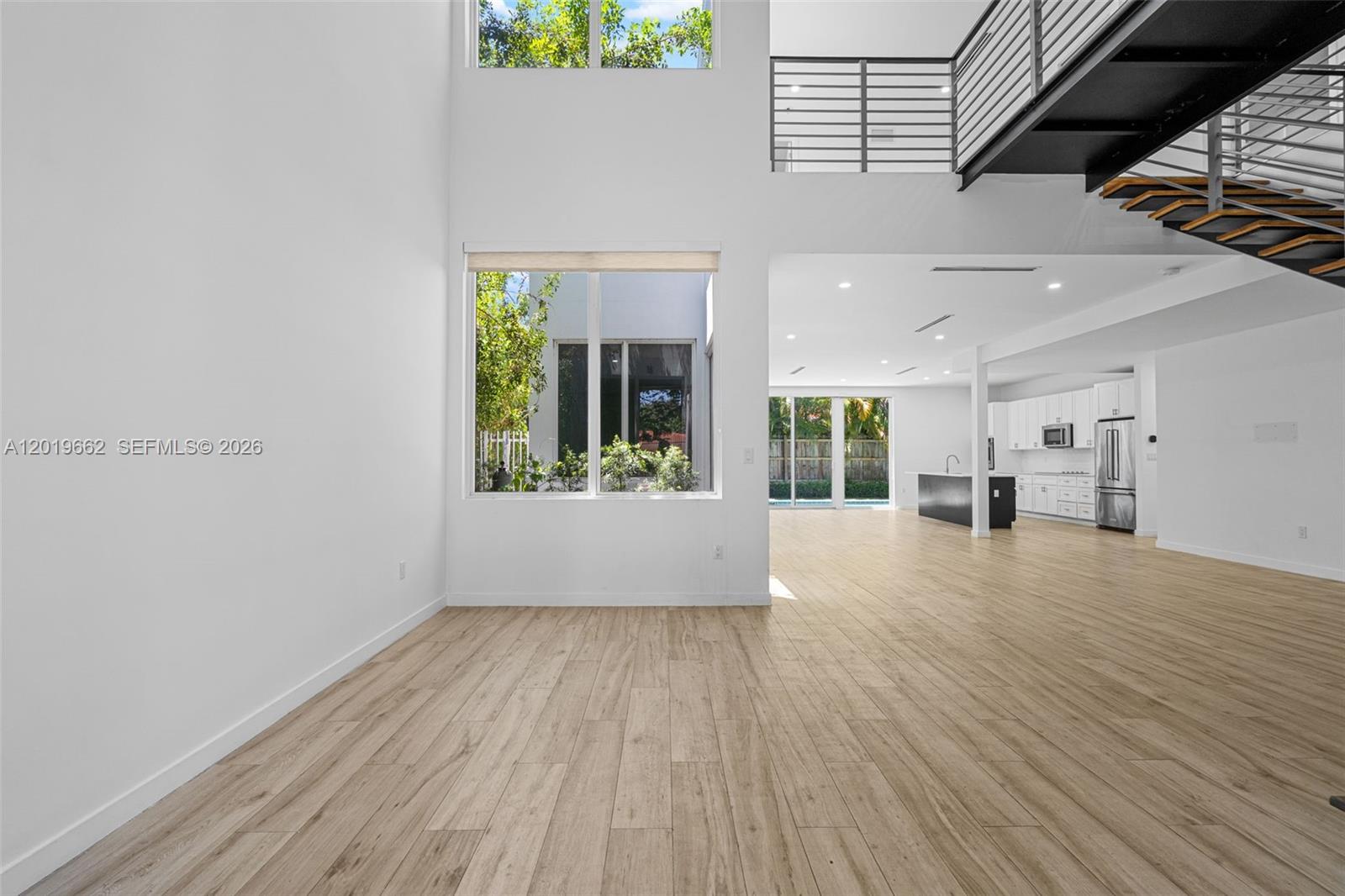 A bright, open-concept living area features light wood-look flooring, a staircase, and a modern kitchen — 1816 SW 23rd St, Miami FL 33145, MIAMI, FL